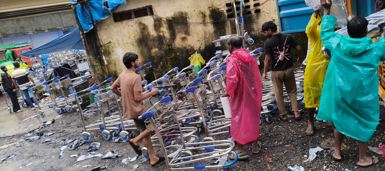 Ground staff loading SS 304 airport luggage trolleys onto delivery truck in rain, Mumbai
